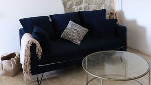 A room with a stone wall, a dark blue sofa, a glass coffee table, and a lamp. - Mas Provençal Rénové Luberon (La Bastide-des-Jourdans)