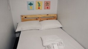 Un lit simple avec une literie blanche, une tête de lit en bois et trois tableaux encadrés accrochés au mur.