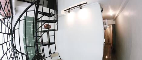 A spiral staircase with a metal railing, a whiteboard, and a folding chair in a hallway.