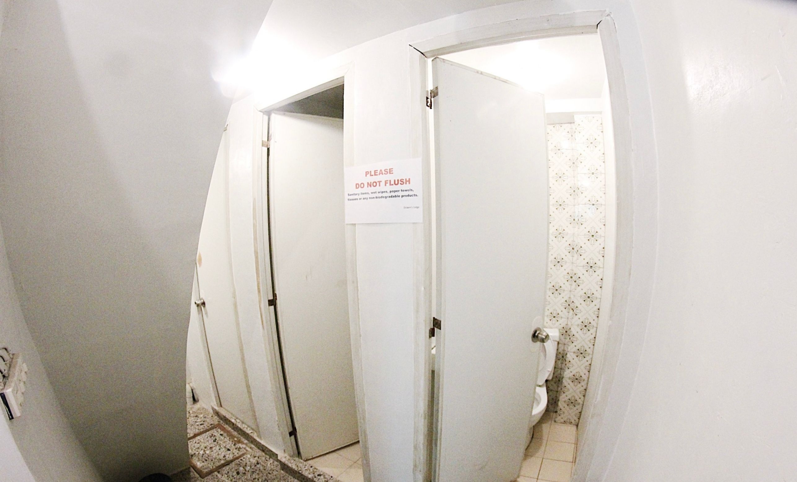 Un pasillo estrecho con tres puertas, una de ellas con un cartel que indica no tirar objetos sanitarios.