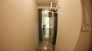 Un couloir étroit doté d’un sol en marbre, d’un appareil de climatisation fixé au mur et d’une porte au fond qui donne sur une autre pièce.
