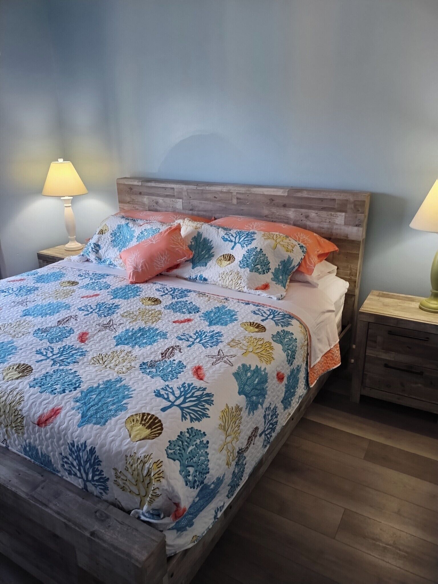 Een bed met een bloemenprint sprei, twee bedlampjes en een houten hoofdeinde.