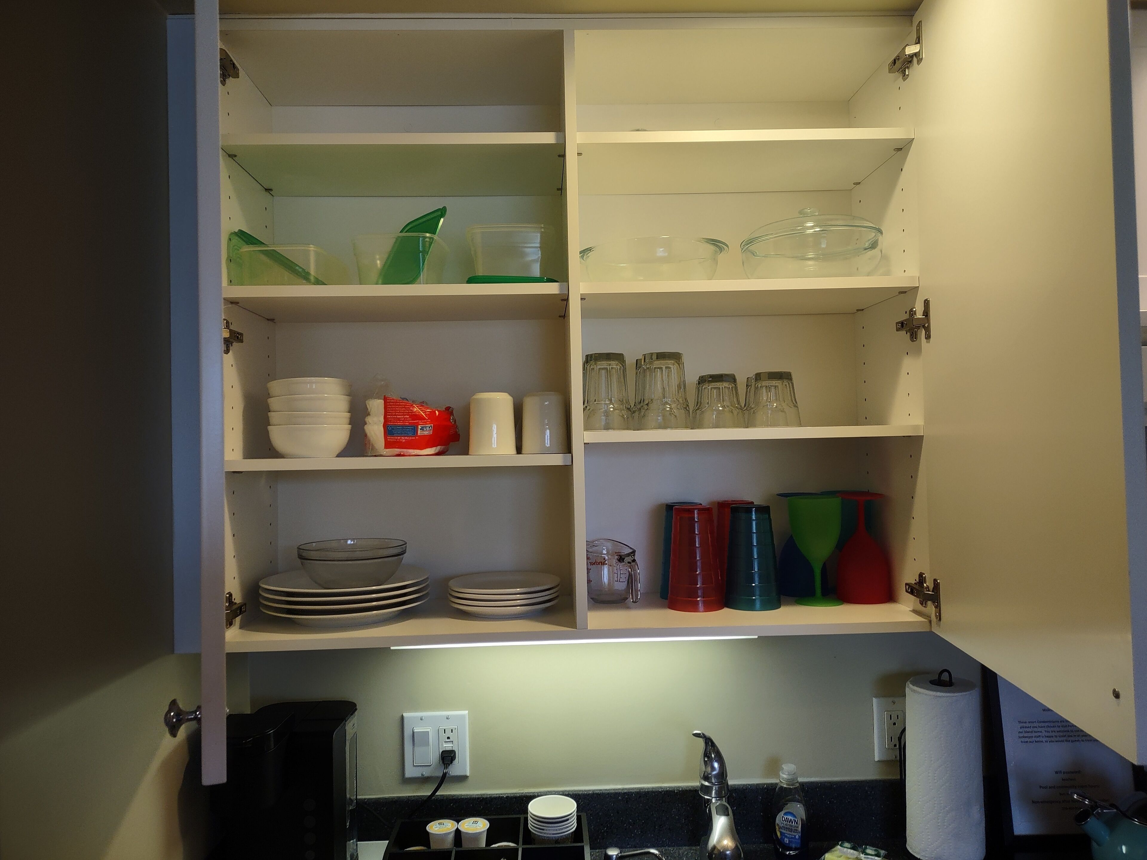 Une cuisine avec des placards ouverts où sont exposés différents plats, verres et récipients.