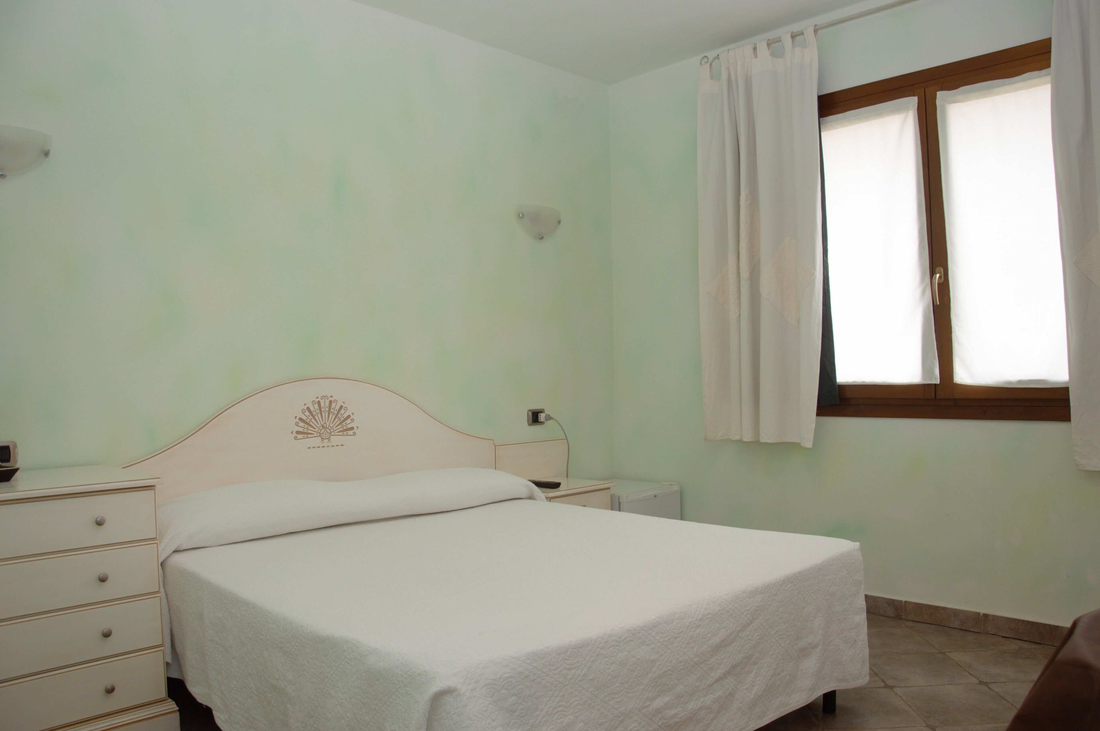 Un dormitorio con una cama individual, una mesita de noche, un aparador y una ventana con cortinas.