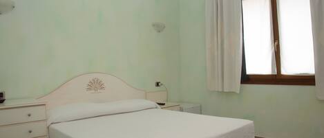 Un dormitorio con una cama individual, una mesita de noche, un aparador y una ventana con cortinas.