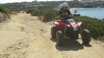 Ein Feldweg führt zu einem Strand, auf dem ein rotes ATV mit zwei Fahrern steht.