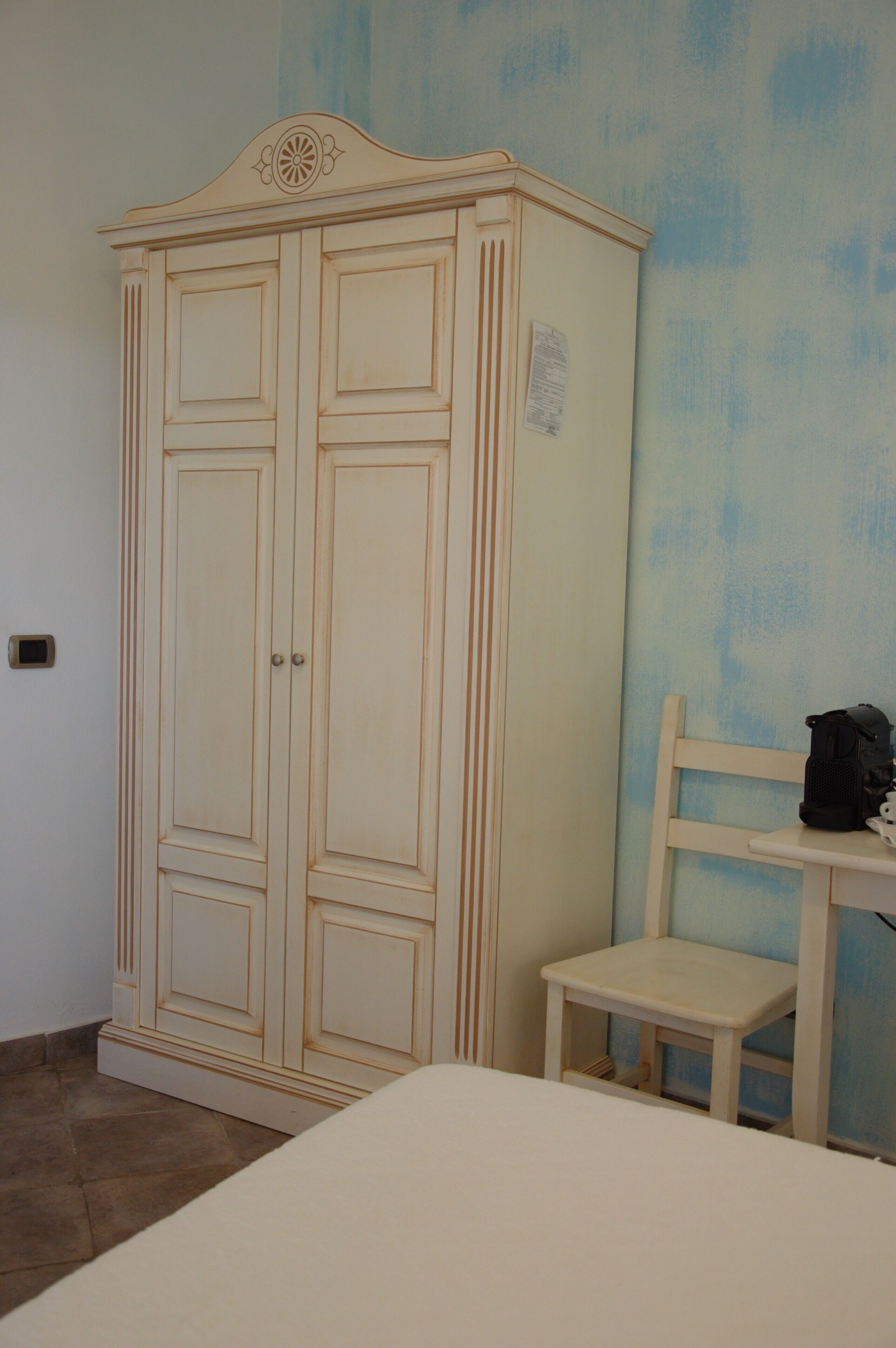 A room with a large wardrobe, a small white chair, and a bed.