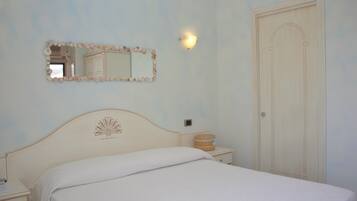 A bedroom with a bed, a nightstand, a mirror with a seashell frame, a wall-mounted light, and a door.