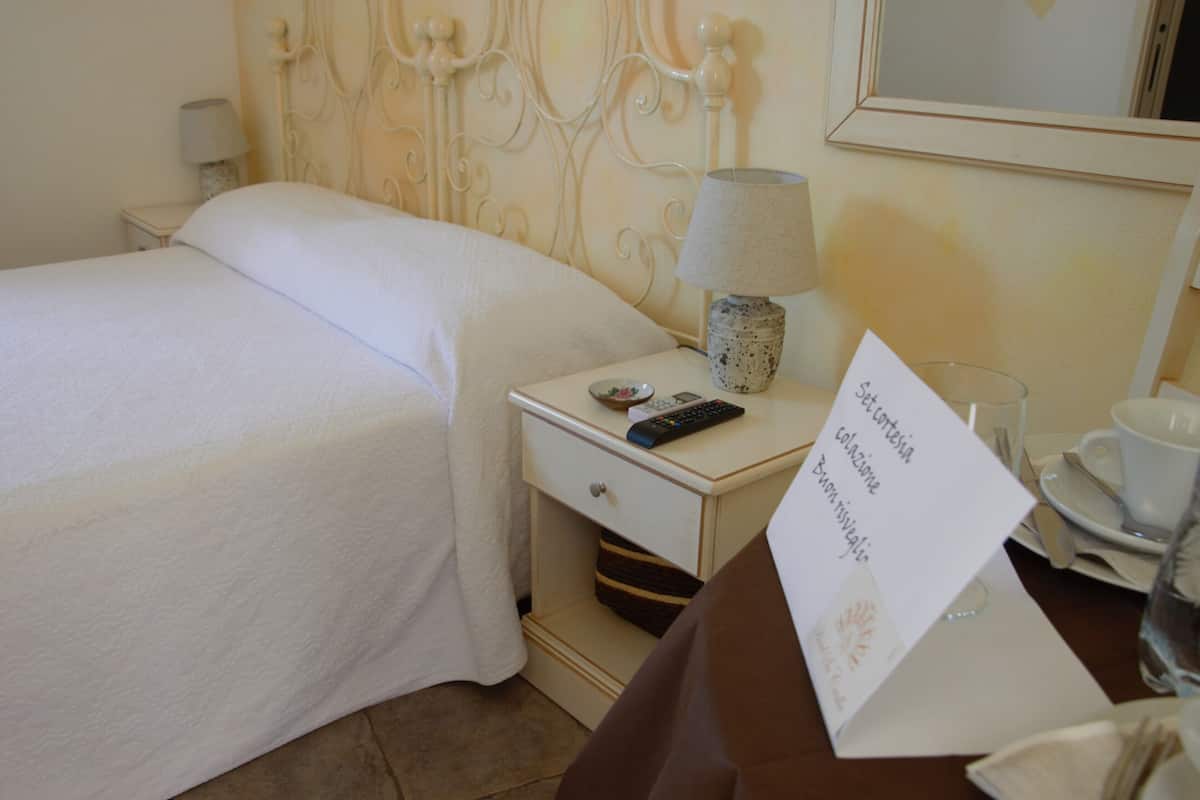 A hotel room with a neatly made bed, a bedside table with a lamp, a remote control, a glass of water, and a menu card.