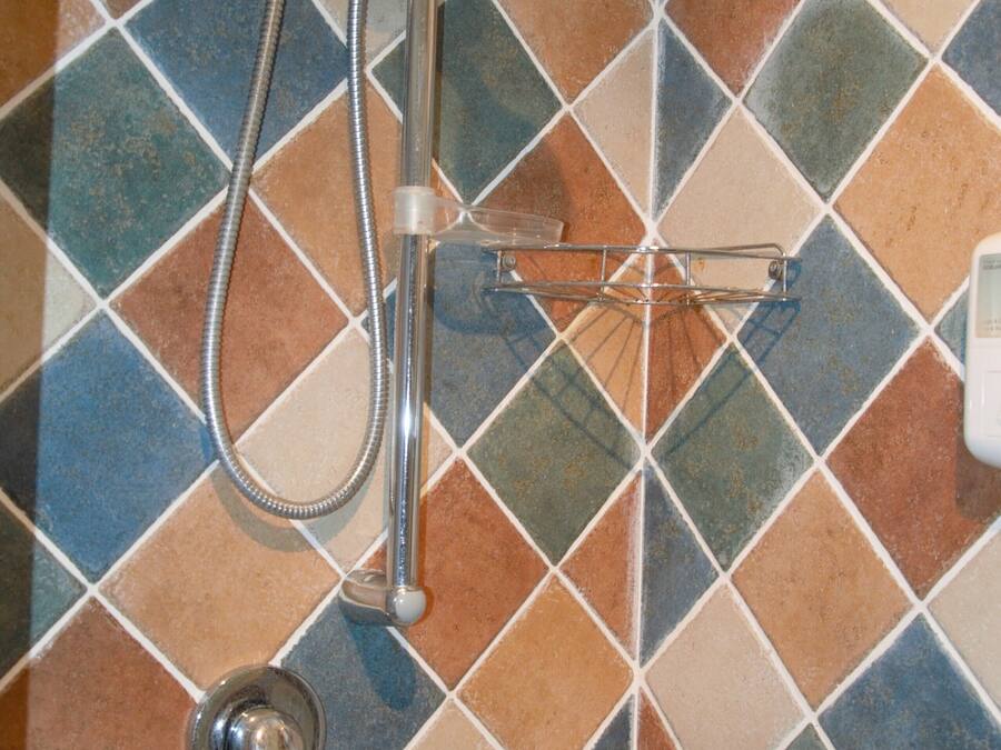 Una ducha con manguera de mano y cabezal de ducha empotrado, frente a una pared de azulejos con diseño de rombos.