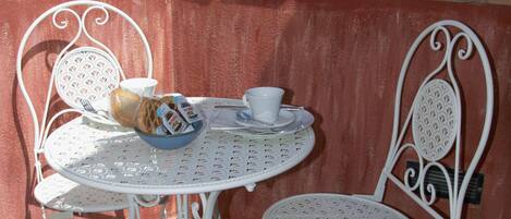 A white metal table and chairs on a terrace with a view of mountains and a red-roofed building in the background.