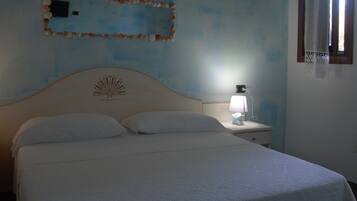 A bedroom with a bed, a nightstand with a lamp, a wall decoration, and a window with a curtain.