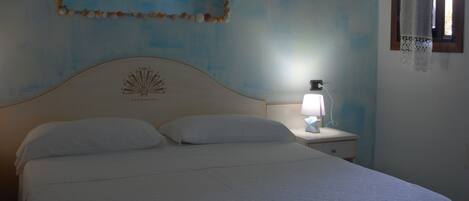 Une chambre à coucher avec un lit, une table de chevet avec une lampe, un élément de décoration murale et une fenêtre avec un rideau.