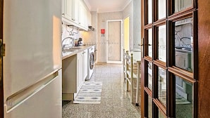A narrow hallway with a washing machine, a small table, and a door leading to another room. - CANIÇO CENTER APARTMENT (Santa Cruz)