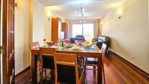 A dining area with a wooden table set for four, surrounded by chairs. A chandelier hangs from the ceiling, and there is a window providing natural light. - CANIÇO CENTER APARTMENT (Santa Cruz)