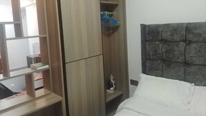 Een hotelkamer met een bed, een garderobe met spiegel en een plank met een strijkijzer.