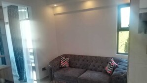 Een moderne woonkamer met een grijze bank, twee decoratieve kussens, een glazen salontafel en uitzicht op een balkon.