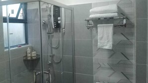 Een douche met glazen wand, een bedieningspaneel, een handdoekrek met opgevouwen handdoeken en een raam met uitzicht.