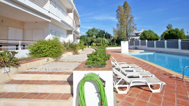 Zona junto a la piscina con vista despejada, escalones que llevan a un edificio y un jardín verde.