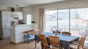 Eine moderne Küche mit weißen Schränken, ein Essbereich mit Holztischen und -stühlen sowie große Fenster mit Blick auf die Stadt.