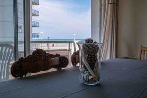 A table with a clear vase containing pinecones and seashells, a vintage car-shaped object, and a view of the beach and ocean through large windows. - Duplex Idéalement Situé Face à la mer (Neufchâtel-Hardelot)