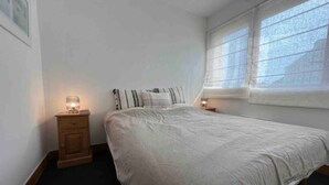 Ein Schlafzimmer mit einem Bett, einem Nachttisch mit Lampe und einem Fenster mit Jalousien.