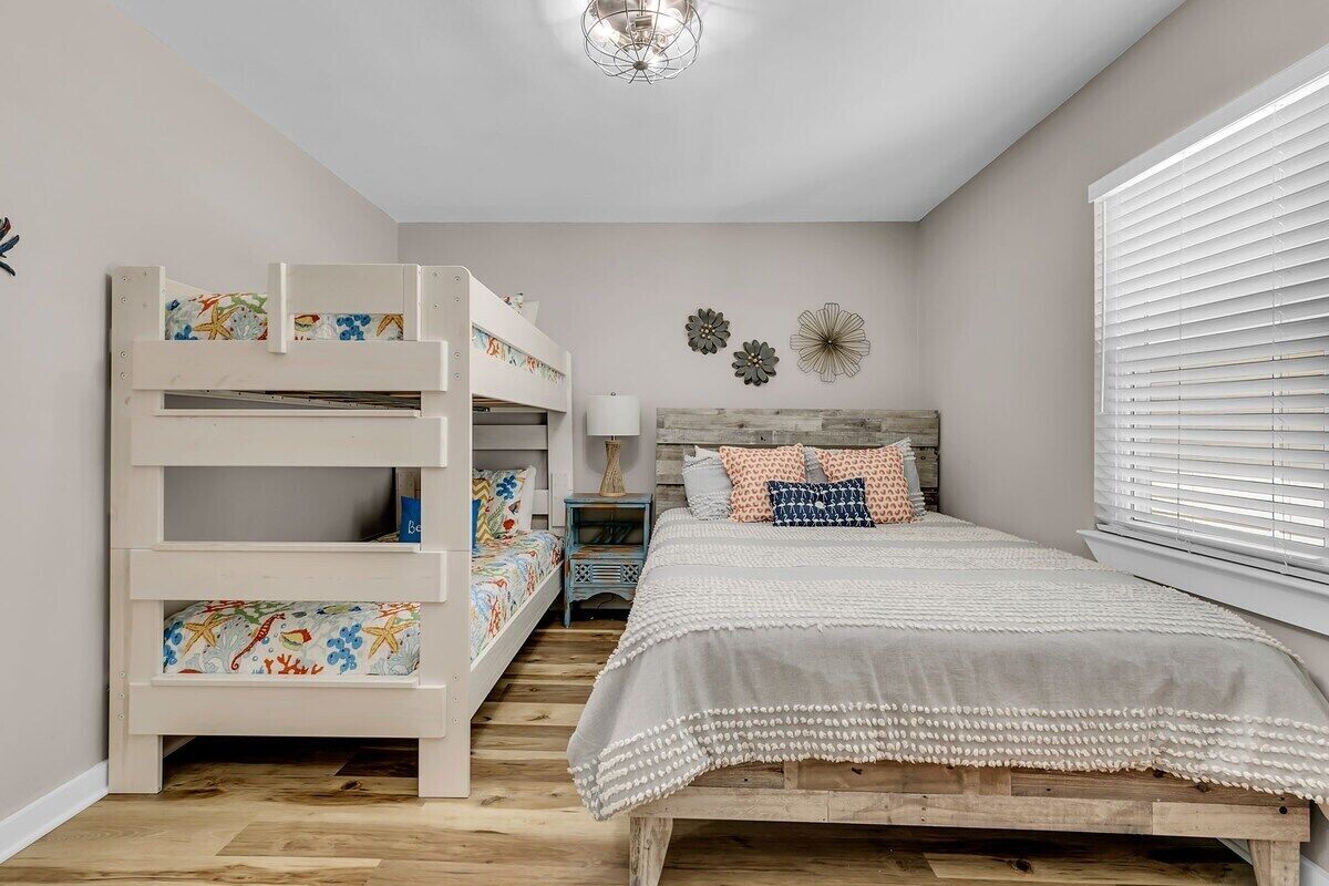 Ein Schlafzimmer mit Etagenbett, einem Bett mit weißer und grauer Bettdecke, einem Holz-Kopfteil und einem Fenster mit Jalousien.