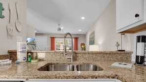Una cocina moderna con encimeras de granito, un lavamanos de acero inoxidable y un ventilador de techo.