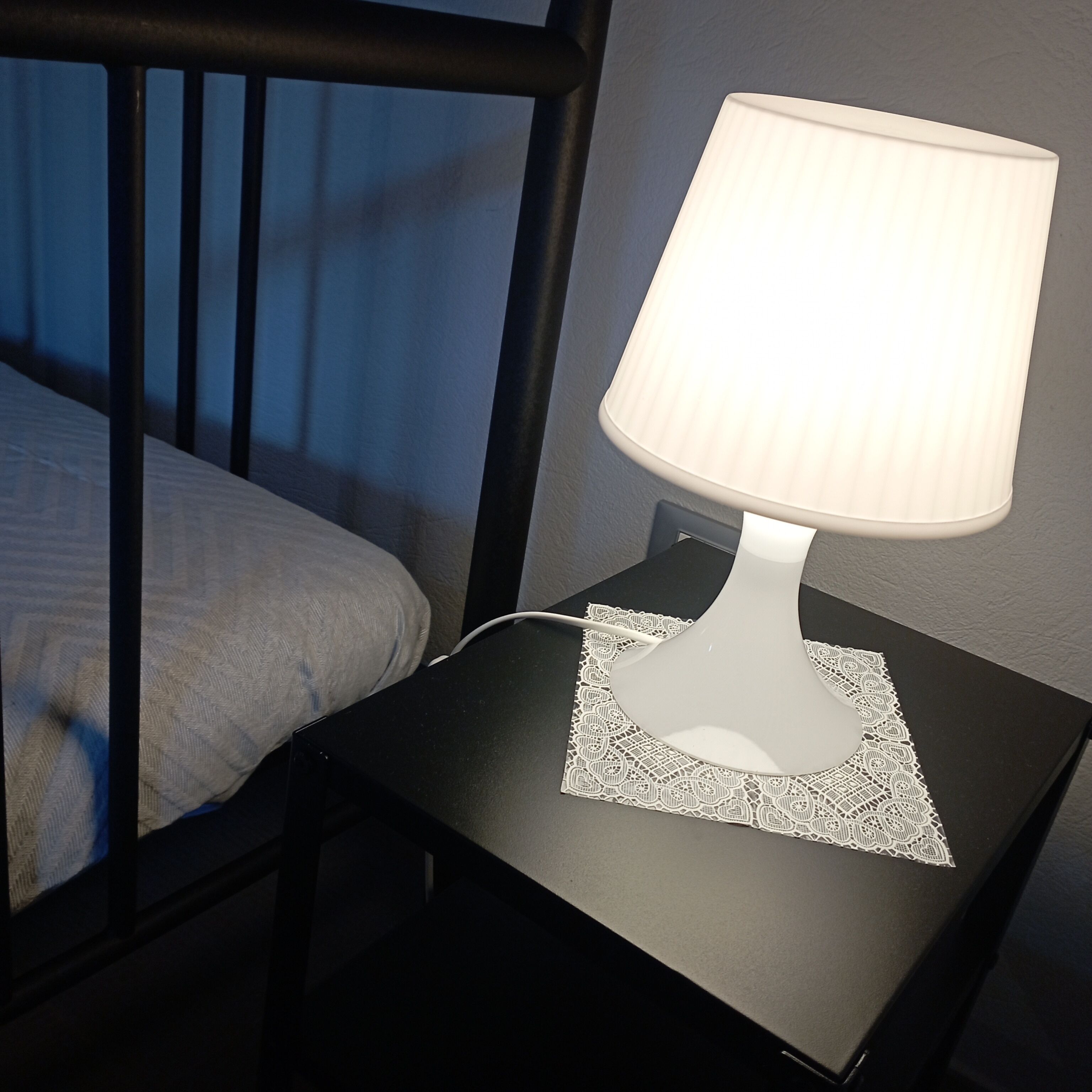 Una mesita de noche con una lámpara y un camandula de encaje.