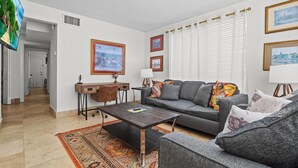 A living room with a sofa, coffee table, and a TV. There are framed pictures on the wall and a window with blinds. - "Davis Islands Charm! Euro Oasis Walkable to Events, Eats & Care!" (Tampa)