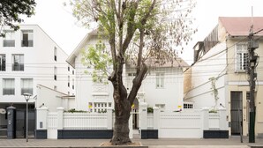 A tree-lined street with white buildings, a gated entrance, and a clear road.