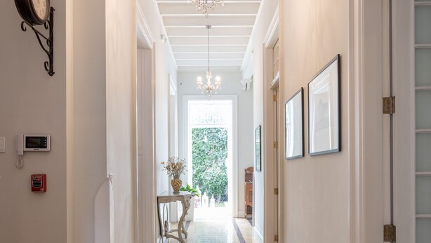 A hallway with a chandelier, a clock, and framed pictures on the walls.