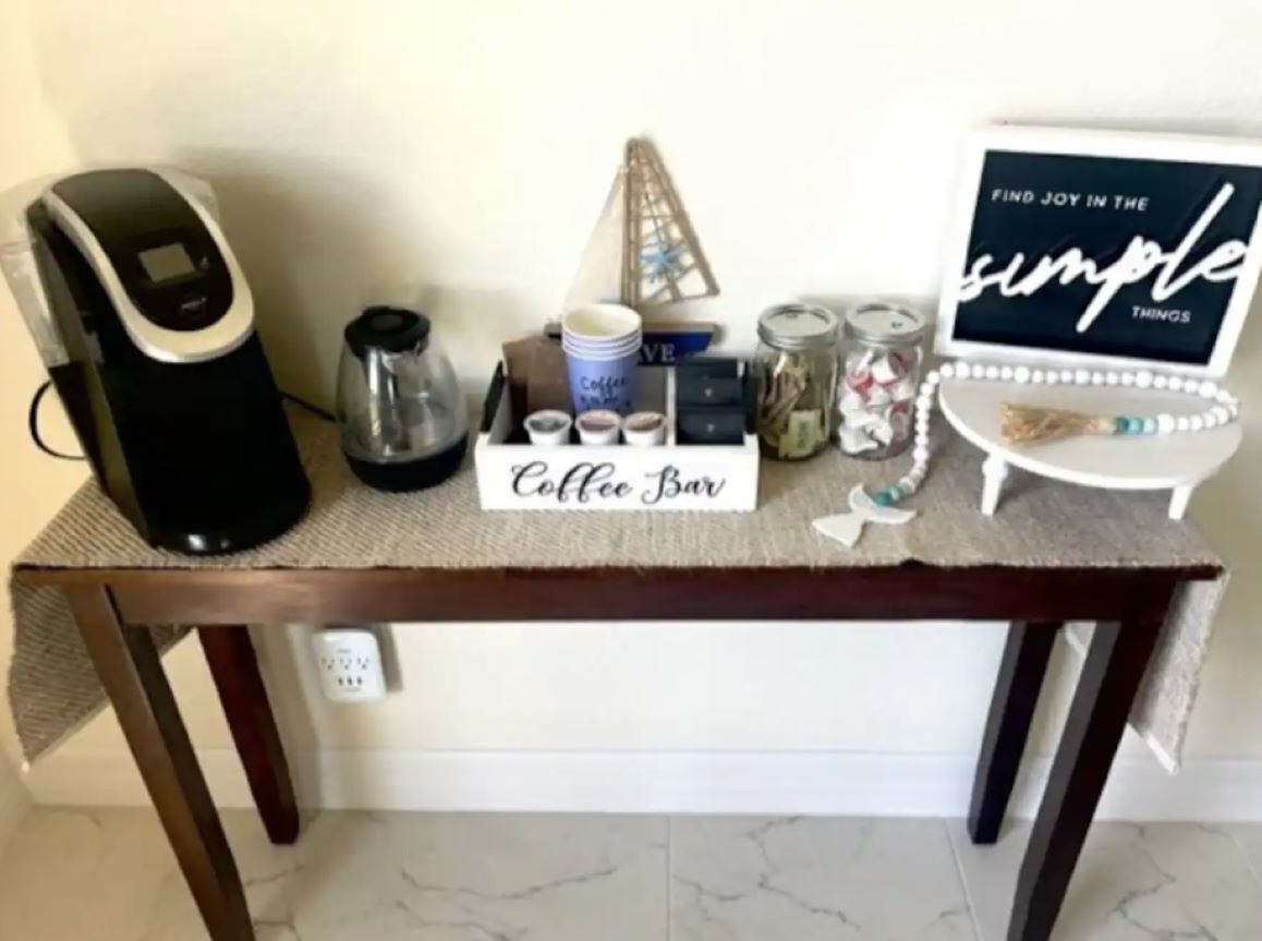 En kaffestation med en kaffebryggare, koppar, burkar och en skylt med texten ”Kaffebar”.