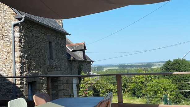 Une terrasse en bois avec une table et des chaises, un bâtiment en pierre en arrière-plan et une vue dégagée sur la campagne.