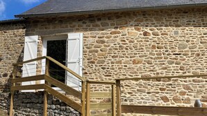 Un bâtiment en pierre avec un escalier en bois menant à une porte dotée de volets blancs.
