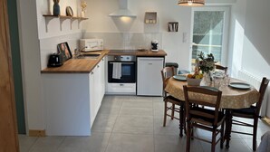 Une cuisine moderne dotée d’un îlot central, d’un four encastré et d’un coin repas avec une table dressée pour quatre personnes.