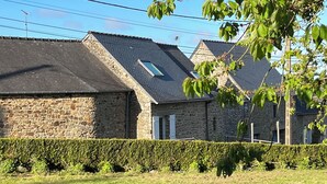 Un bâtiment en pierre avec un toit en pente, une haie devant et un ciel bleu dégagé.