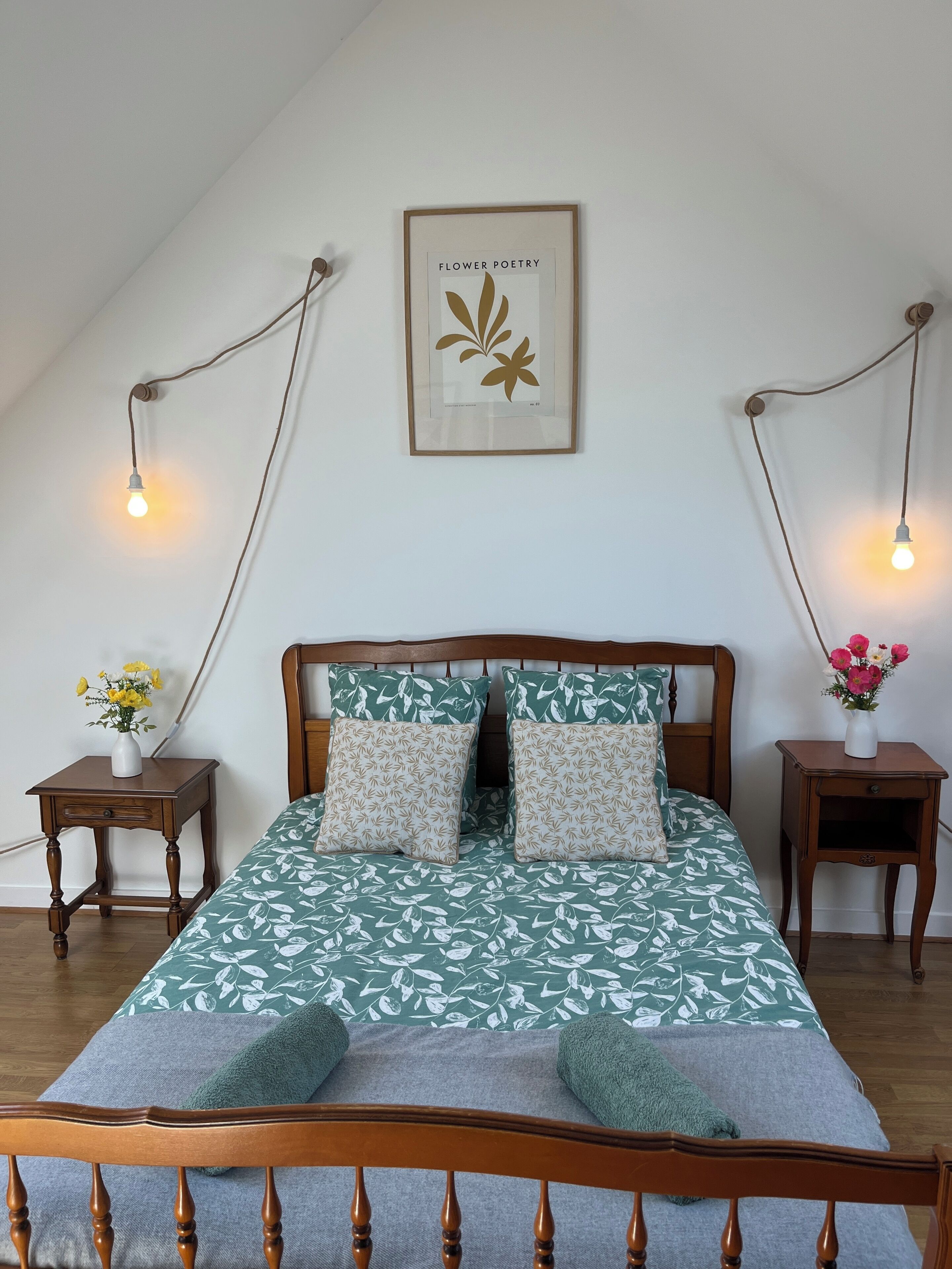 A bedroom with a wooden bed, two bedside tables with lamps, a framed picture on the wall, and a window with a view.