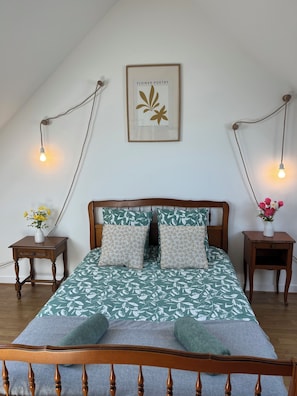 Een slaapkamer met een houten bed, een kunstwerk in een lijst aan de muur en twee nachtkastjes met lampen.