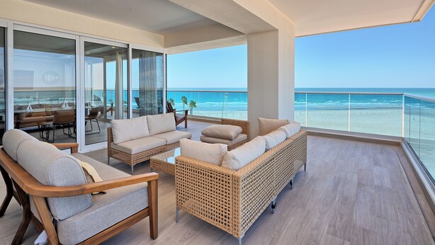 Un balcon avec vue sur l’océan, aménagé avec des canapés en osier et un coin repas.