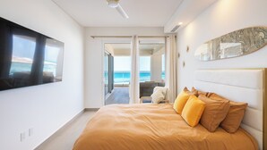 Une chambre moderne avec un grand lit, une vue sur l’océan grâce à une porte coulissante et un téléviseur à écran plat fixé au mur.