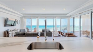Une cuisine moderne dotée d’un grand îlot central, d’un évier intégré et offrant une vue sur la plage.