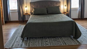Une chambre avec un grand lit, un ventilateur de plafond et deux fenêtres avec des rideaux.