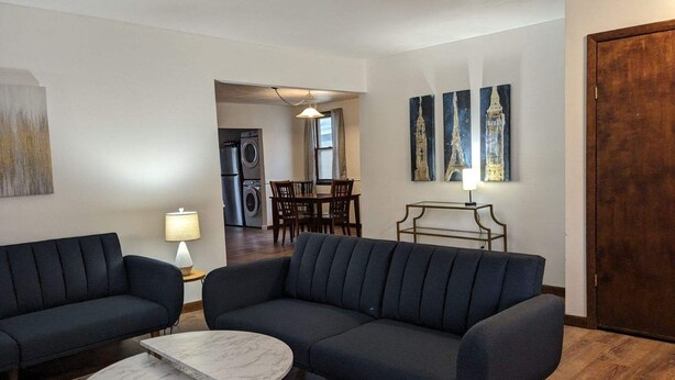 Un salon moderne avec un canapé bleu foncé, une table basse en marbre et un coin repas agrémenté d’un lustre.