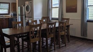 Un coin repas avec une table et des chaises en bois, un lave-linge et, au fond, une cuisine.