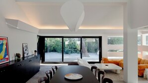 Un espace repas moderne, doté d’une grande table, de chaises et offrant une vue sur l’extérieur grâce à de larges fenêtres.