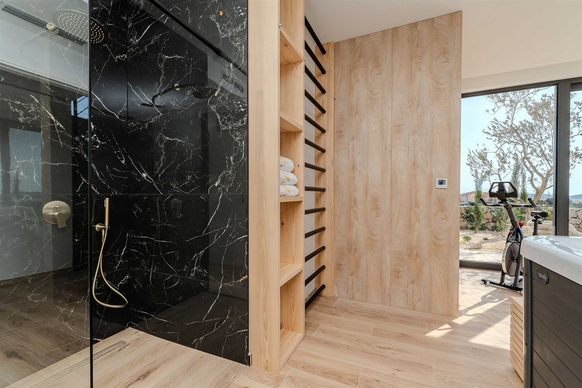 A modern bathroom with a black marble shower, wooden shelving, and a view of the outdoors.
