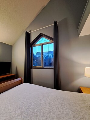 Ett hotellrum med en säng, en tv, ett fönster med gardiner och en lampa.
