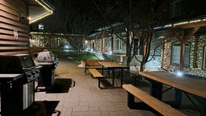 Een terras buiten met picknicktafels en een barbecue.