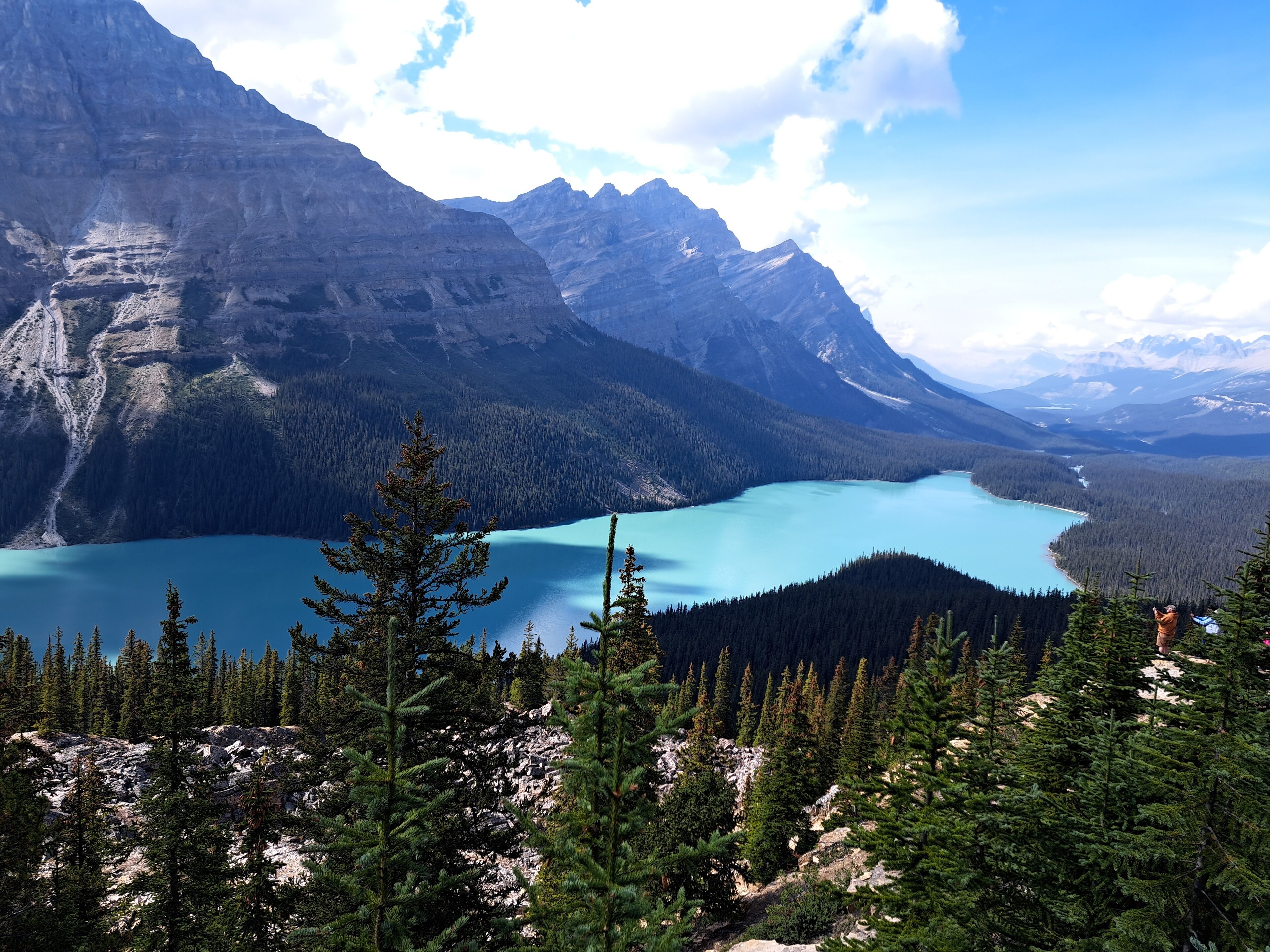 A mountainous landscape with a turquoise lake surrounded by dense forests and rugged peaks.
